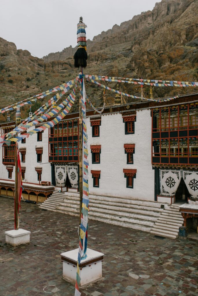 pexels-photo-6576284-6576284 A captivating view of a traditional monastery adorned with colorful prayer flags against a rugged mountainous backdrop.